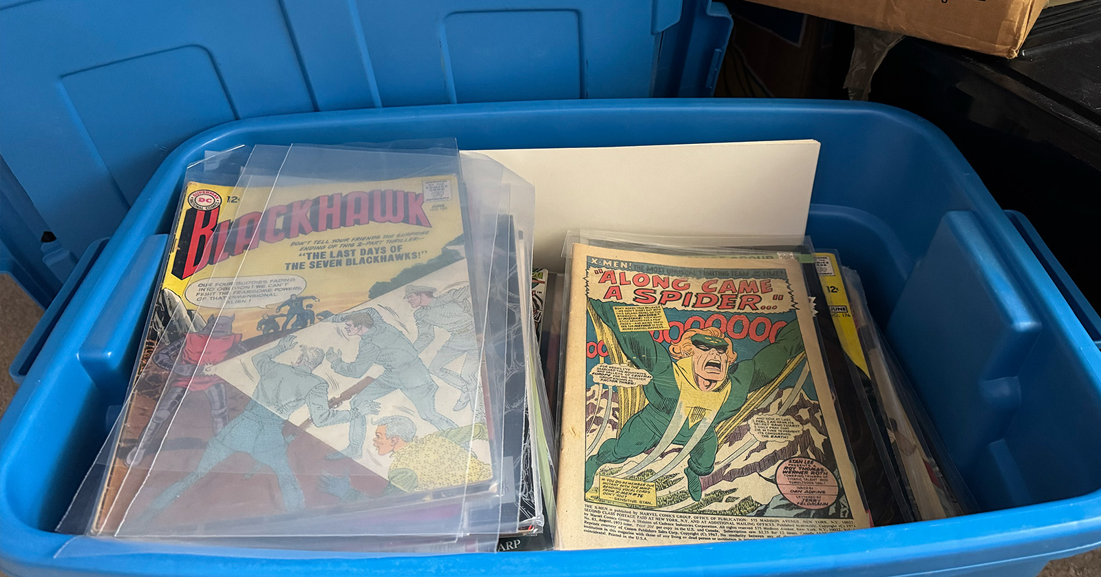 An open storage tote full of old comic books, including worn vintage issues from the 1960s.