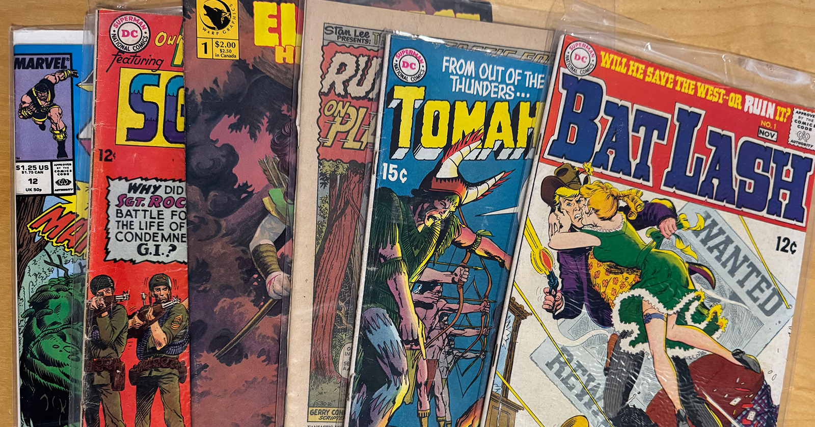 A fanned spread of worn vintage comic books from several decades, including old war, western, and superhero titles.